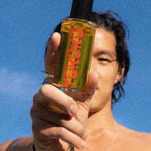 Load image into Gallery viewer, Yokoko Ayurvedic CBD infused Body Oil held in hand by male model under clear blue skies.